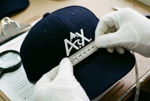A quality control inspector with white gloves checking the stitching on a custom hat, ensuring AQL standards.