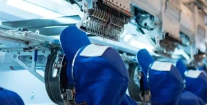 Industrial embroidery machines stitching blue caps in a Custom Hat Manufacturer facility, showing high-volume production capacity.