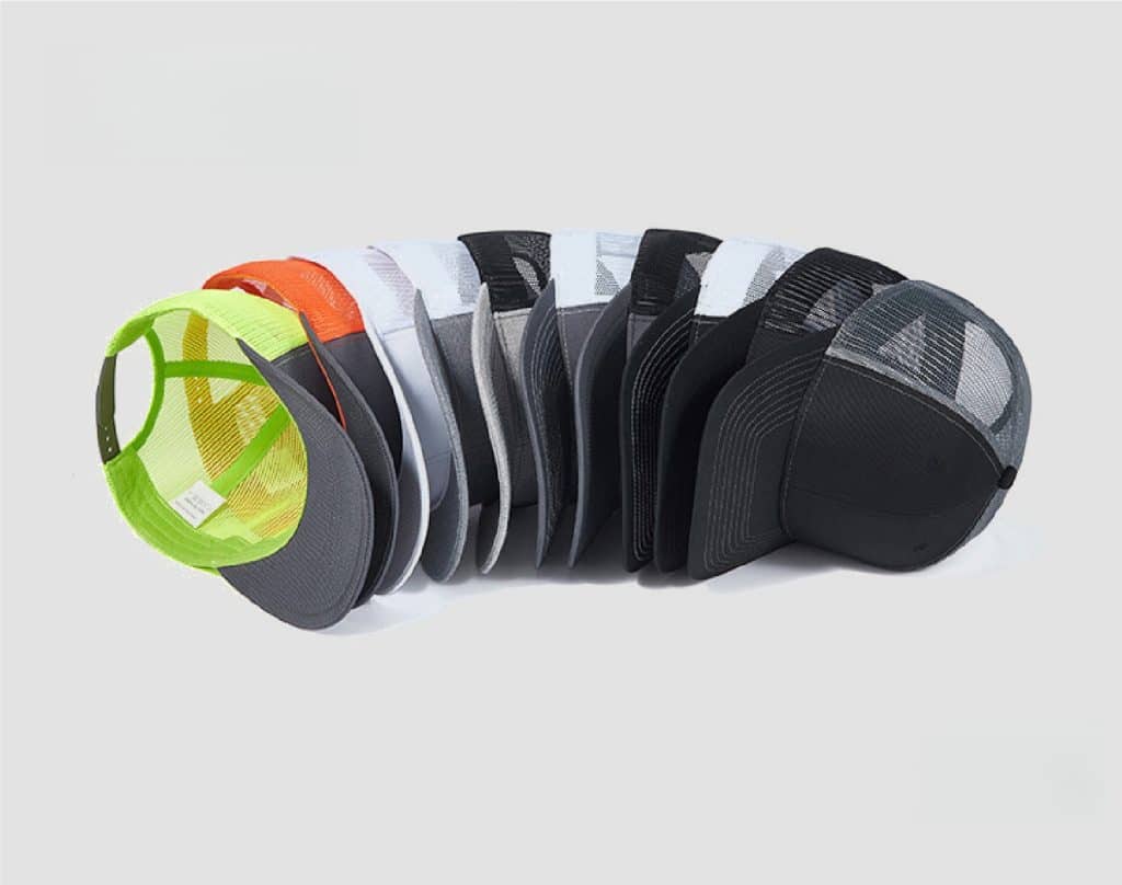 A dynamic fanned-out arrangement of multi-colored blank trucker hats (neon, orange, grey, black) on a white background, demonstrating US stock variety.